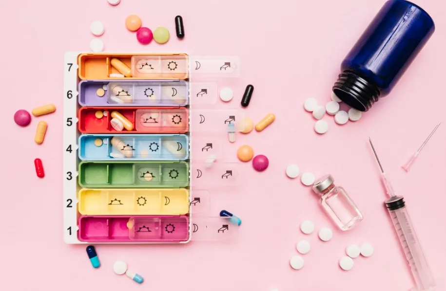 Weekly pill organizer, prescription medications, syringe, and medicine vial arranged for scheduled dosing, illustrating specialty pharmacy medication management and personalized treatment plans.