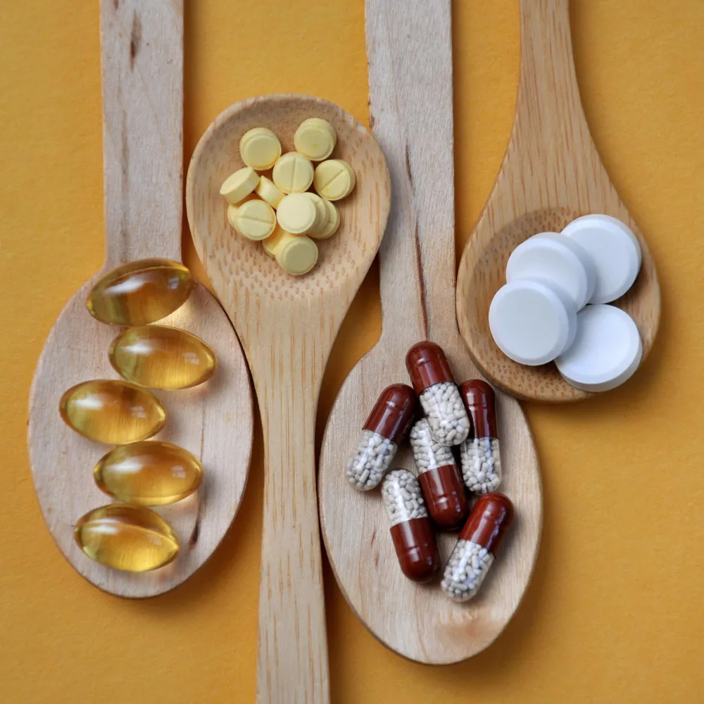 Various capsules, tablets, and softgel nutraceutical supplements arranged in wooden spoons, representing different vitamins and supplement options for daily wellness.