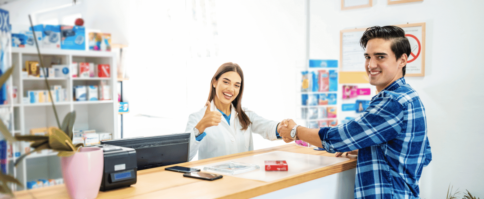 Pharmacist smiling and giving a thumbs-up while assisting a customer at the pharmacy counter, representing professional Pharmacy Clinical Services and patient support.