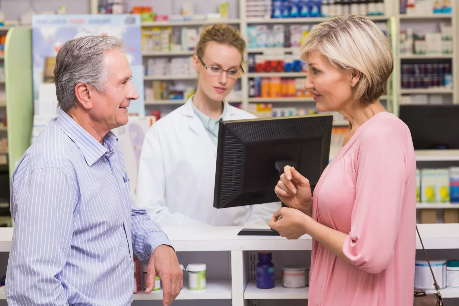 Pharmacist assisting customers at a pharmacy counter, highlighting personalized Medication Sync Solutions that help patients manage and refill prescriptions conveniently through a Pharmacy Refill Sync Program