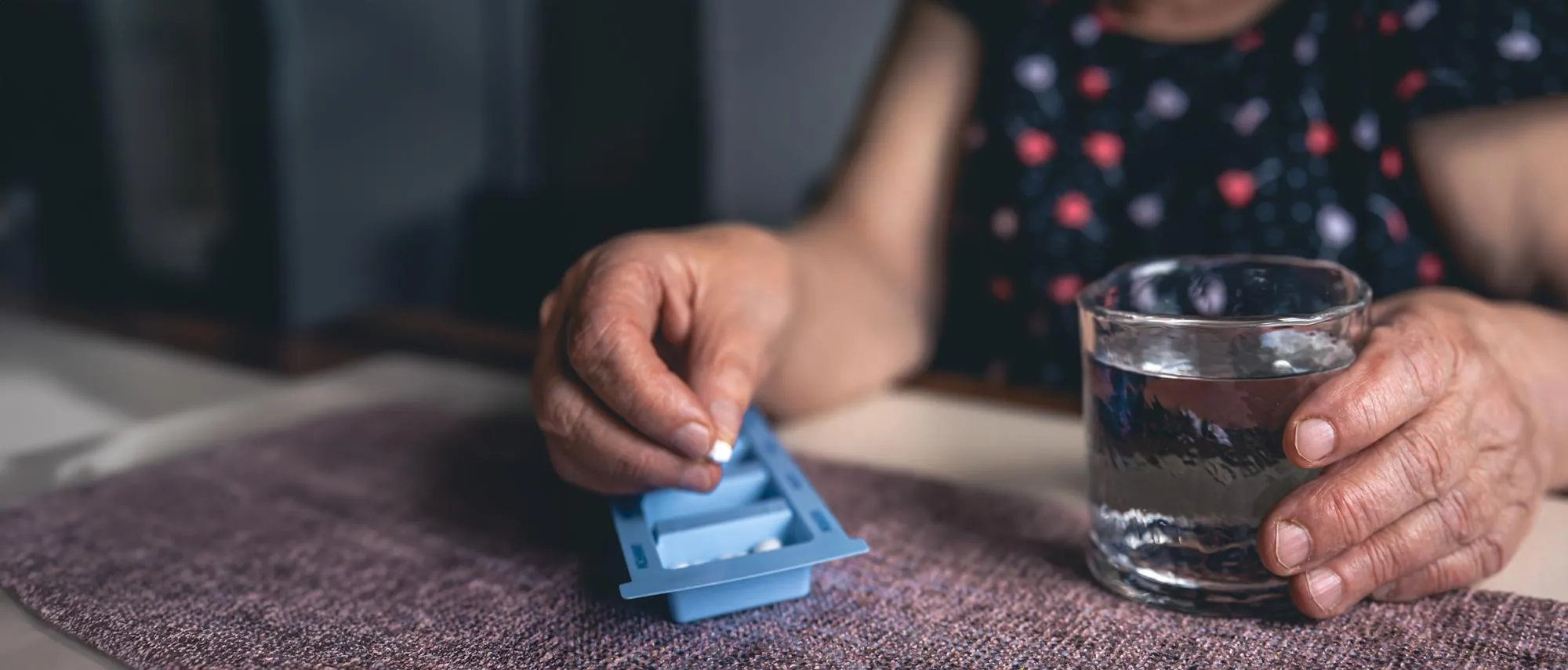 Older adult using a daily pill organizer with a glass of water at home, highlighting how durable medical equipment (DME) and medical supplies support safe medication management and recovery in Jacksonville, FL.