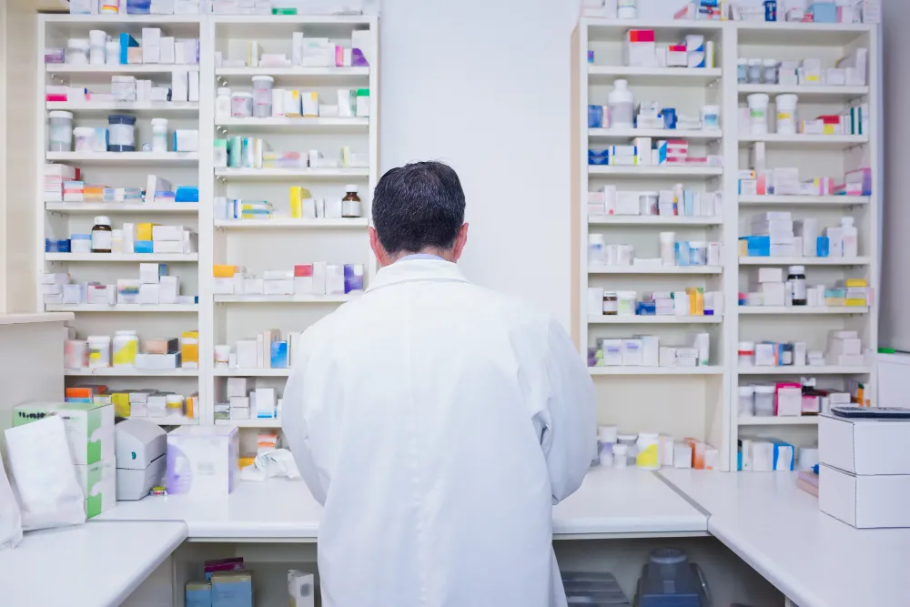 Pharmacist working in a specialty pharmacy medication storage area, preparing high-complexity medication solutions for patients through a family care specialty pharmacy.