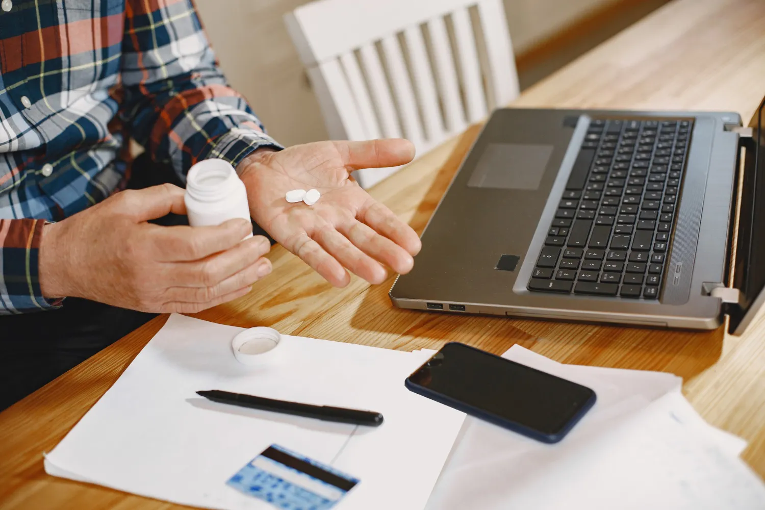Patient holding medication beside a laptop, representing a safe prescription delivery service.
